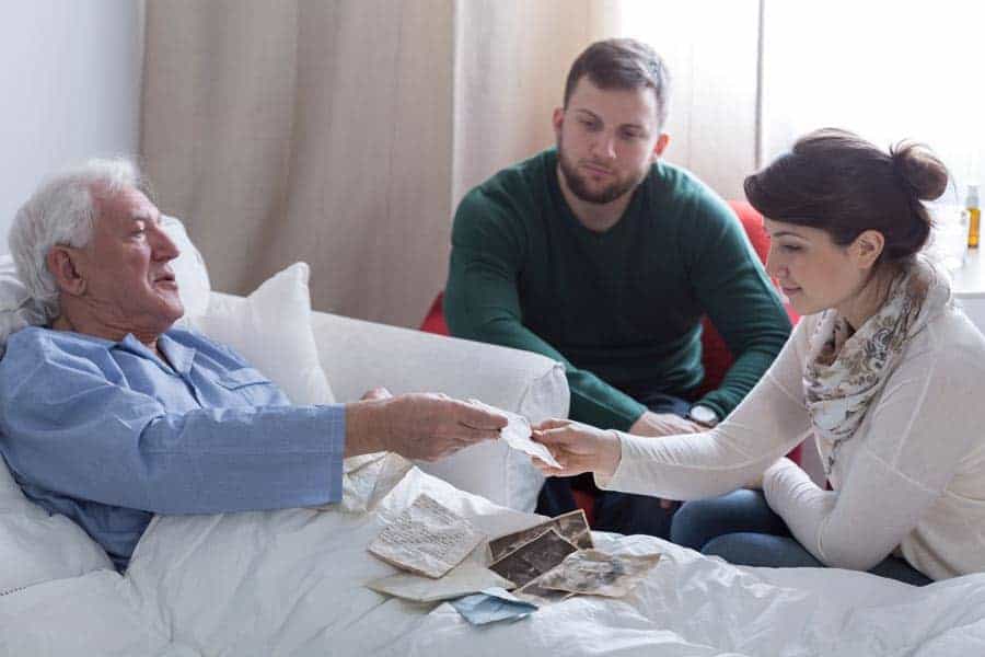 Sick Elderly man in bed being visited by his grown daughter and son.