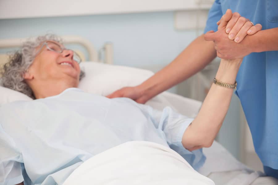 Nurse holding the hand of an older female hospice patient in her hospital bed