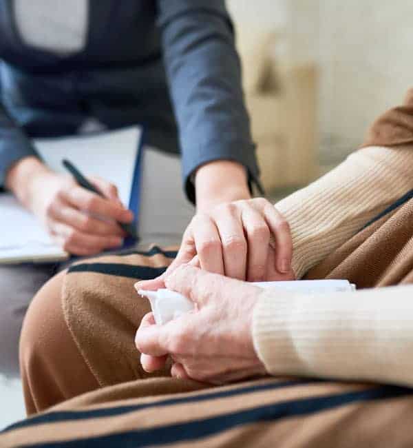 counselor holding the hand of patient. Patient has tissues in hands from crying.