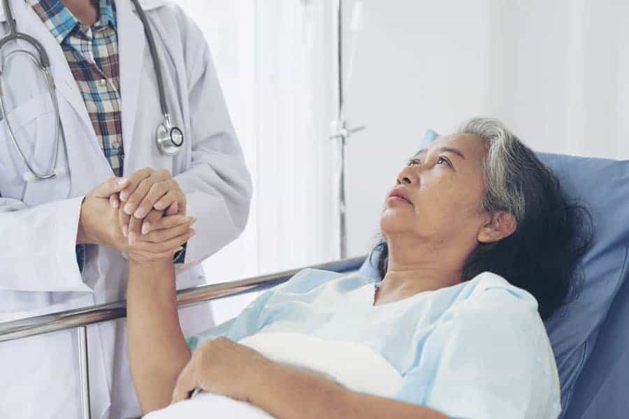 Hospice patient in hospital bed at the Connecticut Hospice holding hands with her doctor