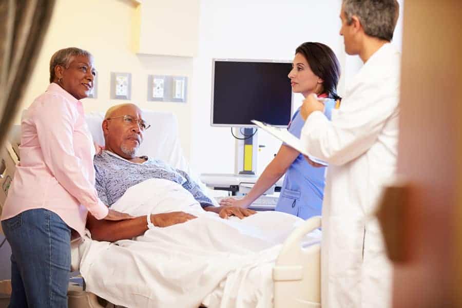 a Palliative care patient in hospital bed with his wife speaking to doctors