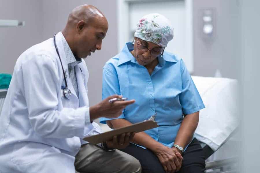 Female Cancer Patient sitting on an exam table looking at a doctor's clip board