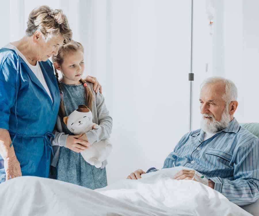 A nurse comforts a little girl beside the sickbed of a hospice patient