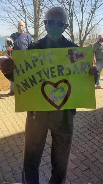 Masked family member holds Happy Anniversary sign up against window for hospice patient at Connecticut Hospice to see.