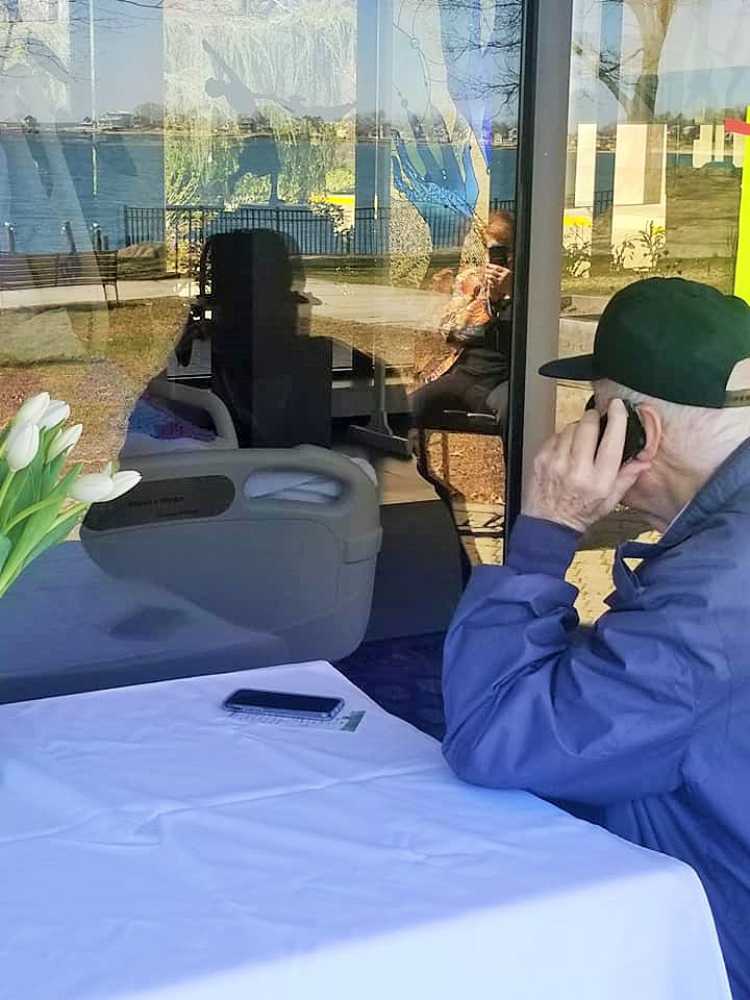 Elderly gentleman talks on phone to hospice patient wife through window