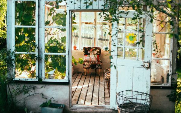 View into a cottage sunroom from outside, with rustic furniture and plants