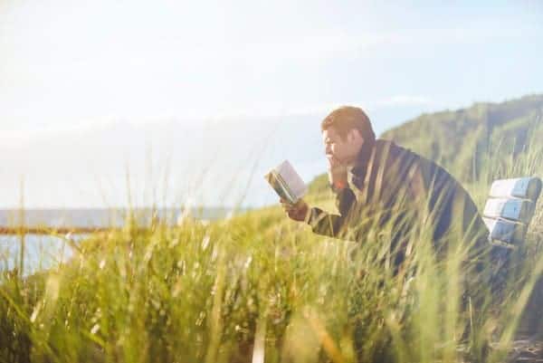 Man reads a book while sitting on bench overlooking the sea