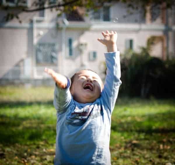 Small child laughs joyfully while reaching up for bubbles