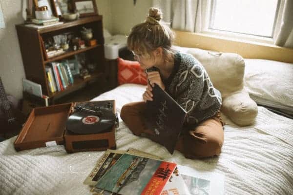 Woman sits on bed listening to albums on portable record player