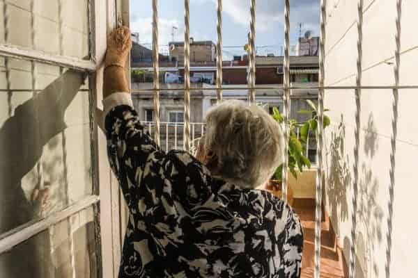 Elderly woman looks outside through iron gateway