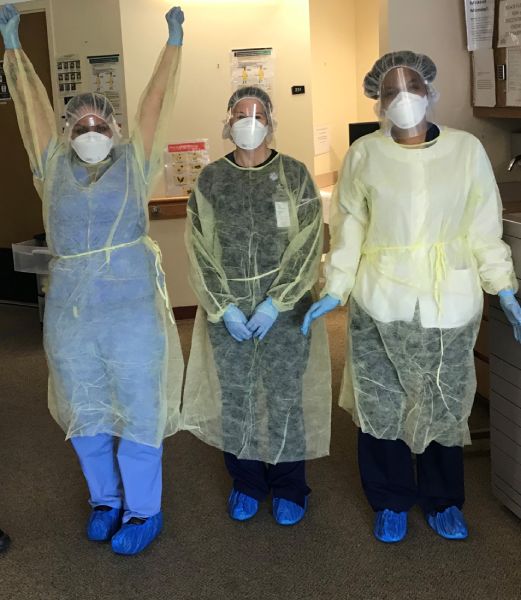 Three nurses at Connecticut Hospice in protective gear smile at the camera, one raises arms in cheer.