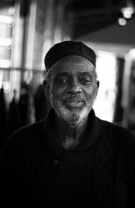 black and white portrait of smiling dark-skinned elder wearing kufi cap