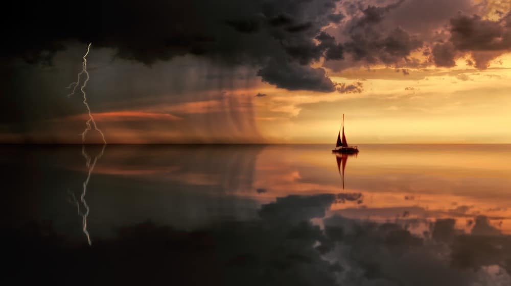 orange sunset with lightening and rain storm in distance, and boat in calm water in foreground