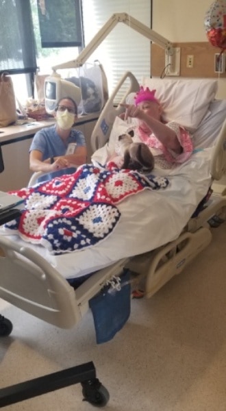 Hospice patient points to tv screen where her out-of-state family members give greetings on her Zoom Birthday Party