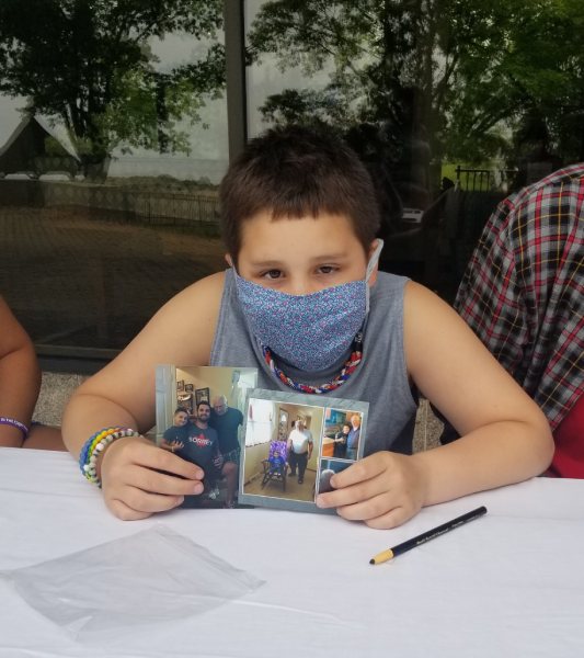 boy wearing mask holds up photos of himself with his great-grandfather