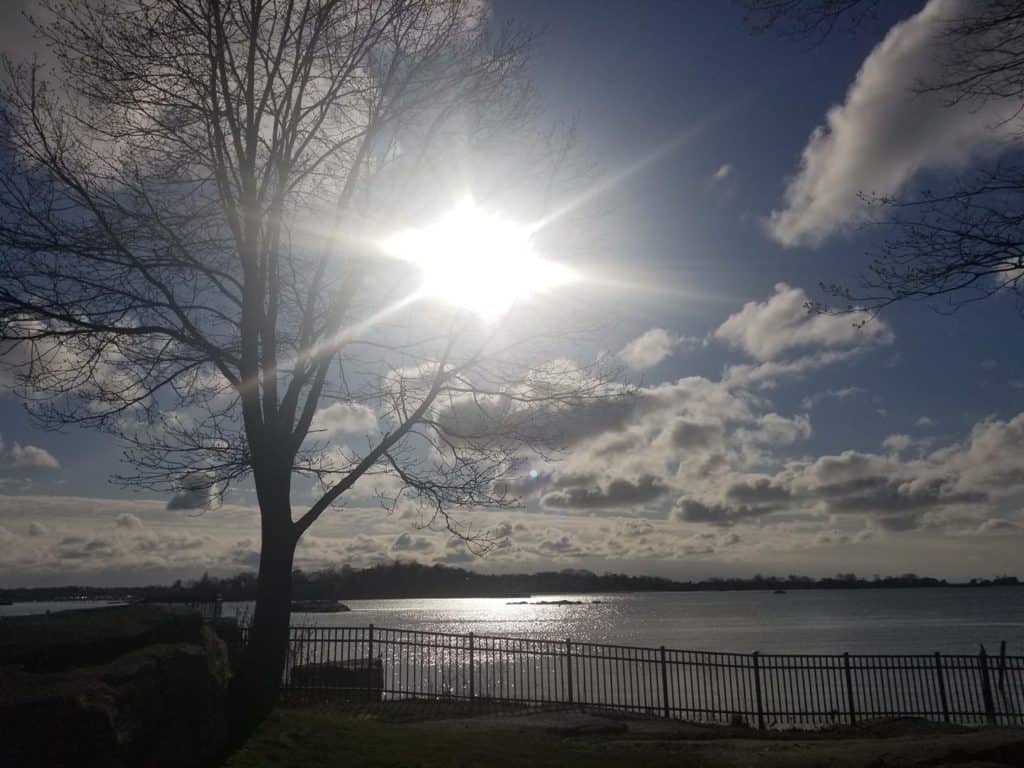 Bright sun breaking through numerous clouds in sky creating bright reflection off water 