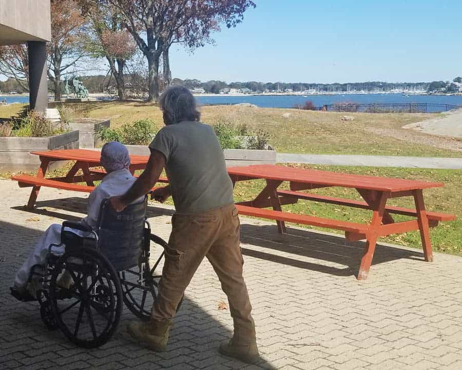Connecticut Hospice volunteer pushes patient in wheelchair so she can enjoy the water views outdoors