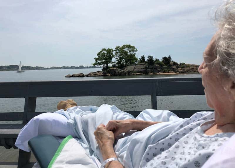 femail patient in hospital bed outside on deck looking at boats on water