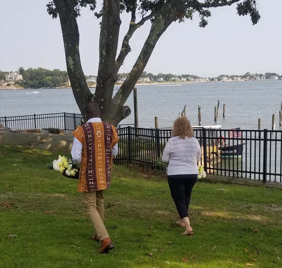 Grieving loved ones walk with flowers to a boat.