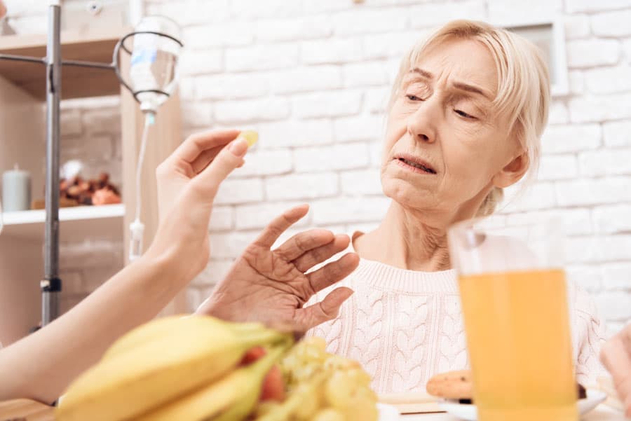 Ederly woman is refusing to eat fruit being offered by a caregiver.