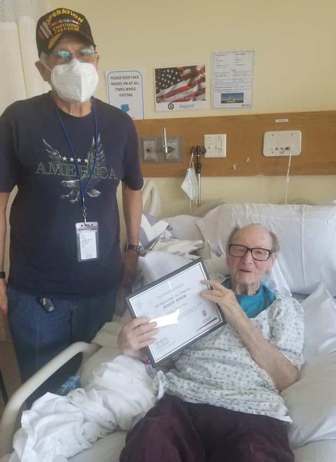 Male Veteran in hospital bed receiving cert from veteran