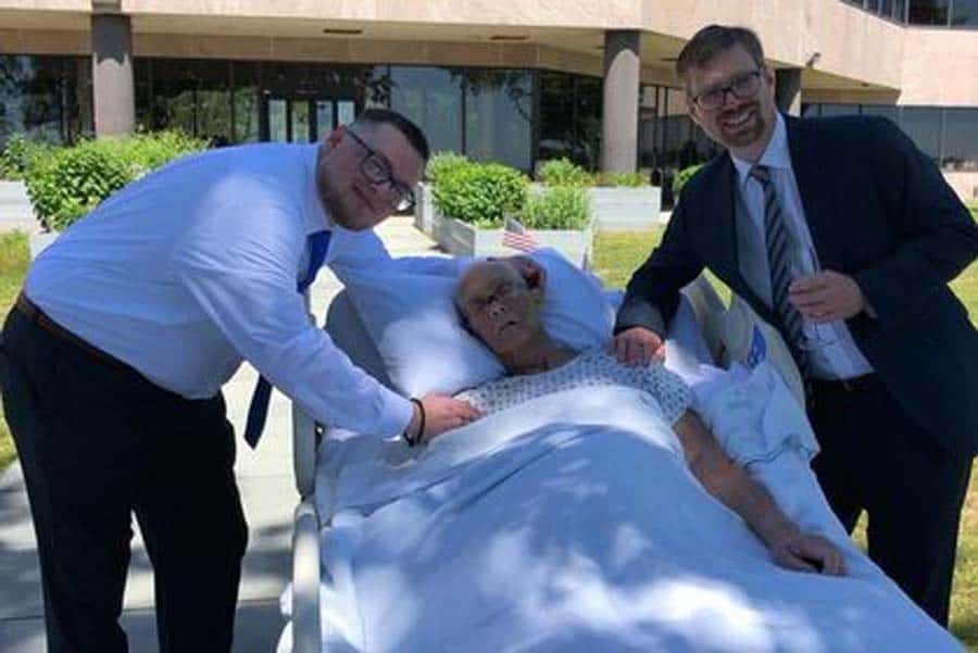 Sons on either side of male hospice patient in bed