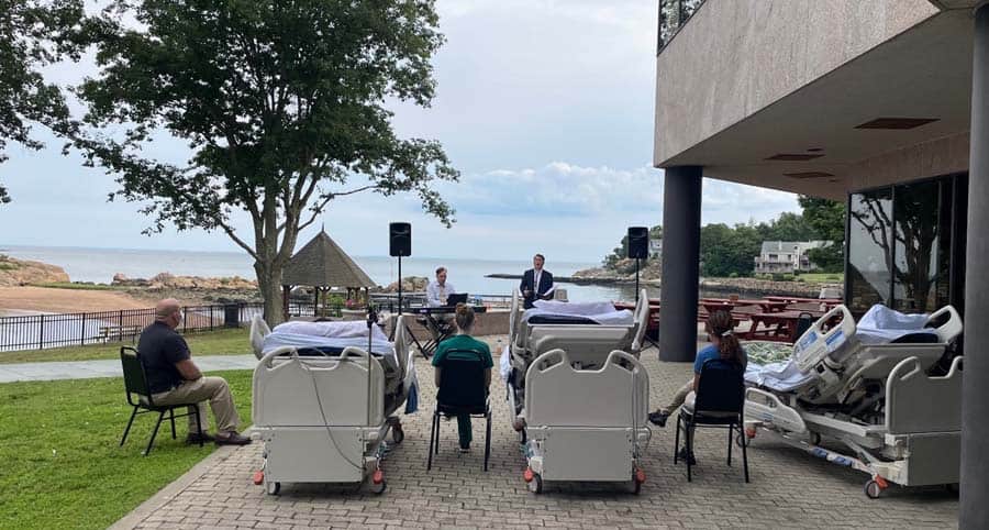 Patients in hospital beds outside watching singers