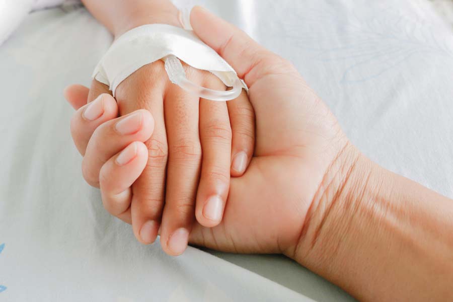 parent hold ind teen hand in hospital bed