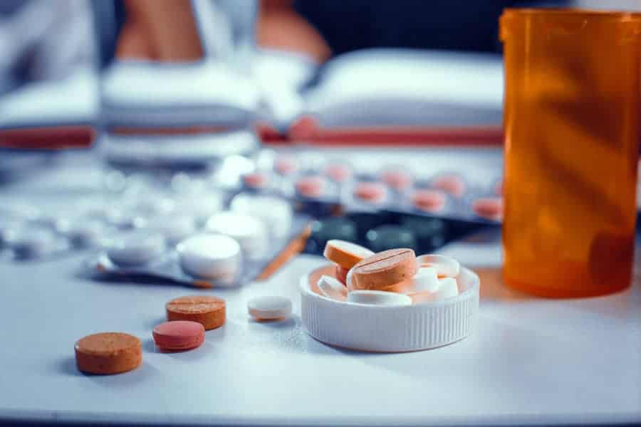 Orange and white tablets are laying on the table. Packs of the pills is in the bottle's cap. Blurred image of tablets packs on the background.