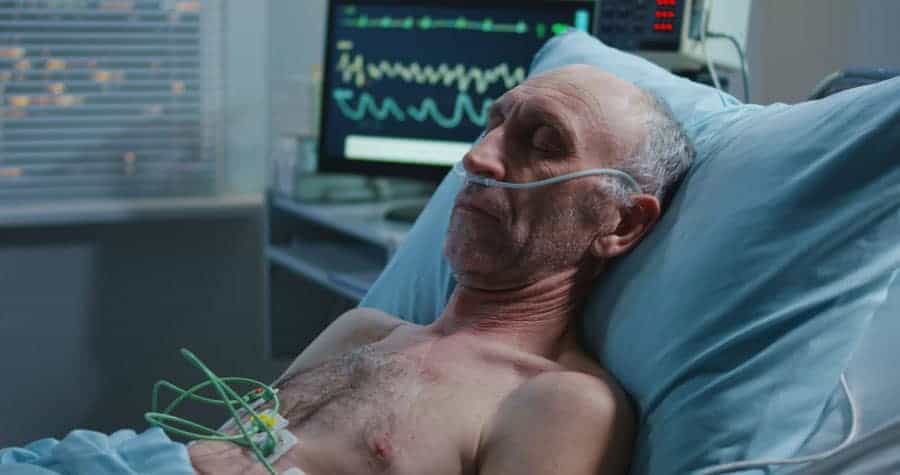 Medium shot of an elderly male patient sleeping and a heart monitor showing vital signs