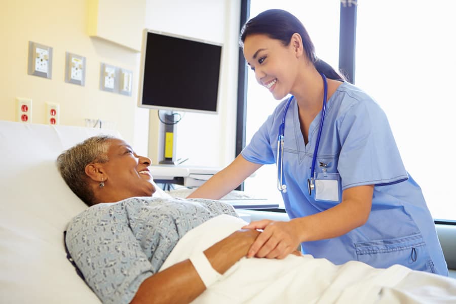 Hospice nurse holding the hands of a female patient in a hospital bed