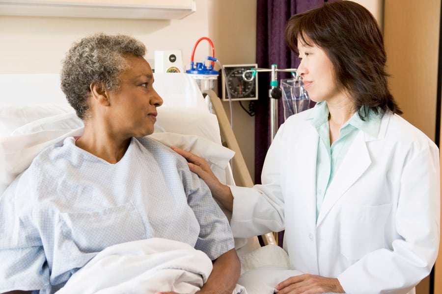 Hospice doctor with hand on the shoulder of a patient in a hospital bed