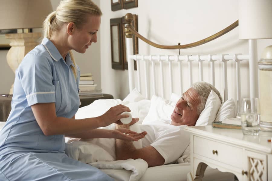 Nurse Giving Senior Male Medication In Bed At Home