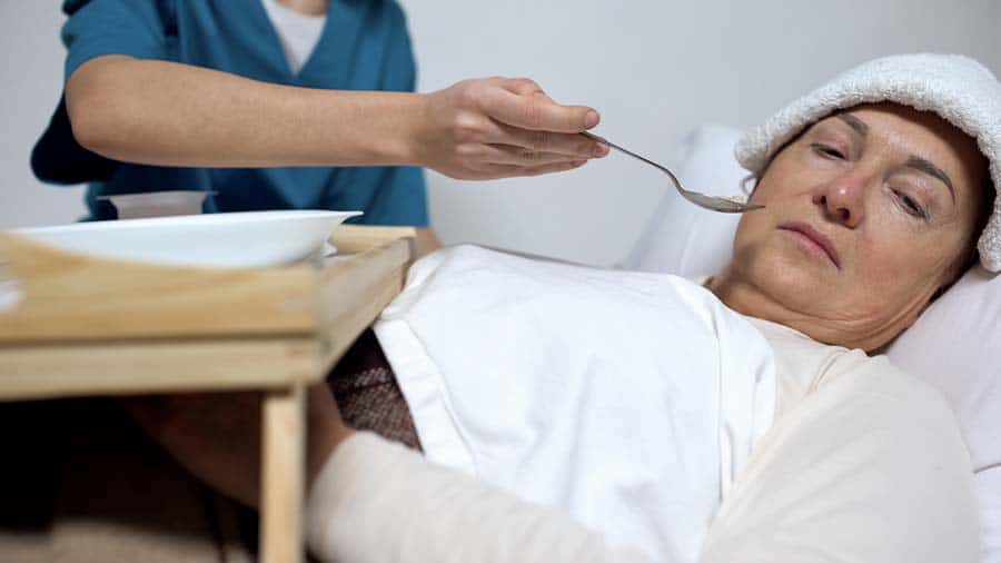 Terminally ill woman with compress on forehead refusing from hospice porridge