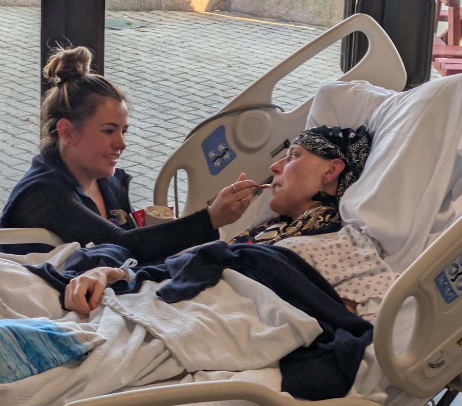 Nurse feeding a bed-bound hospice patient in front or a picture window of the outsied biews. jpg