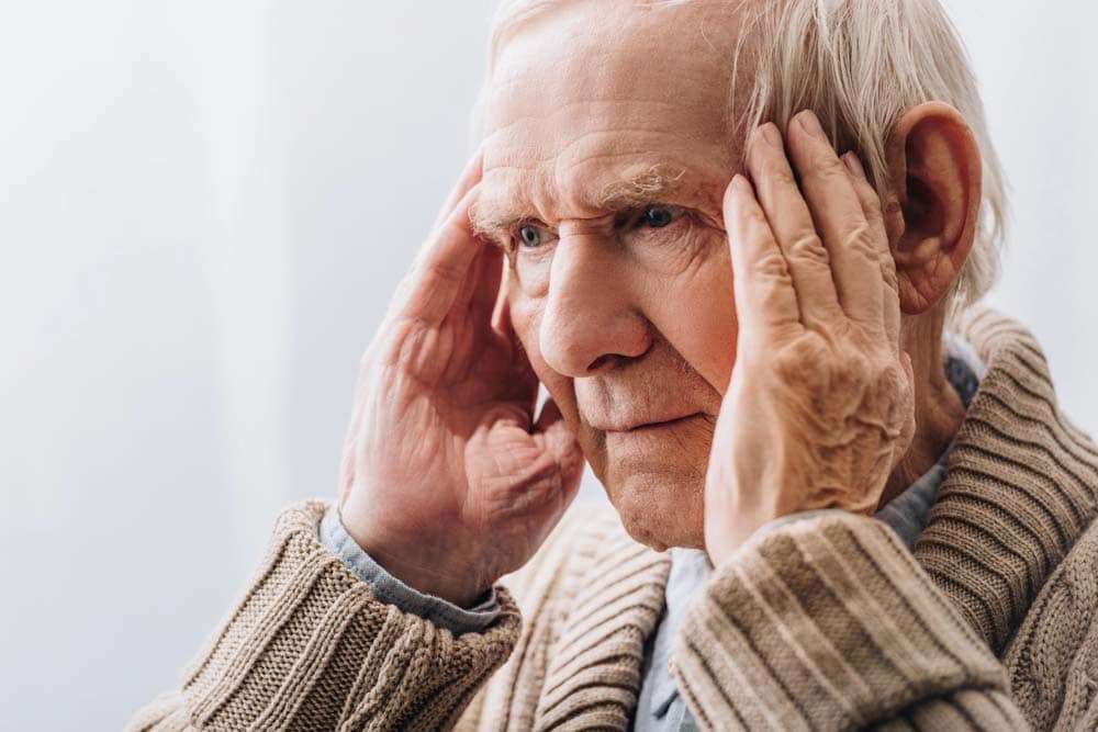 An elderly man holding his head and looking upset
