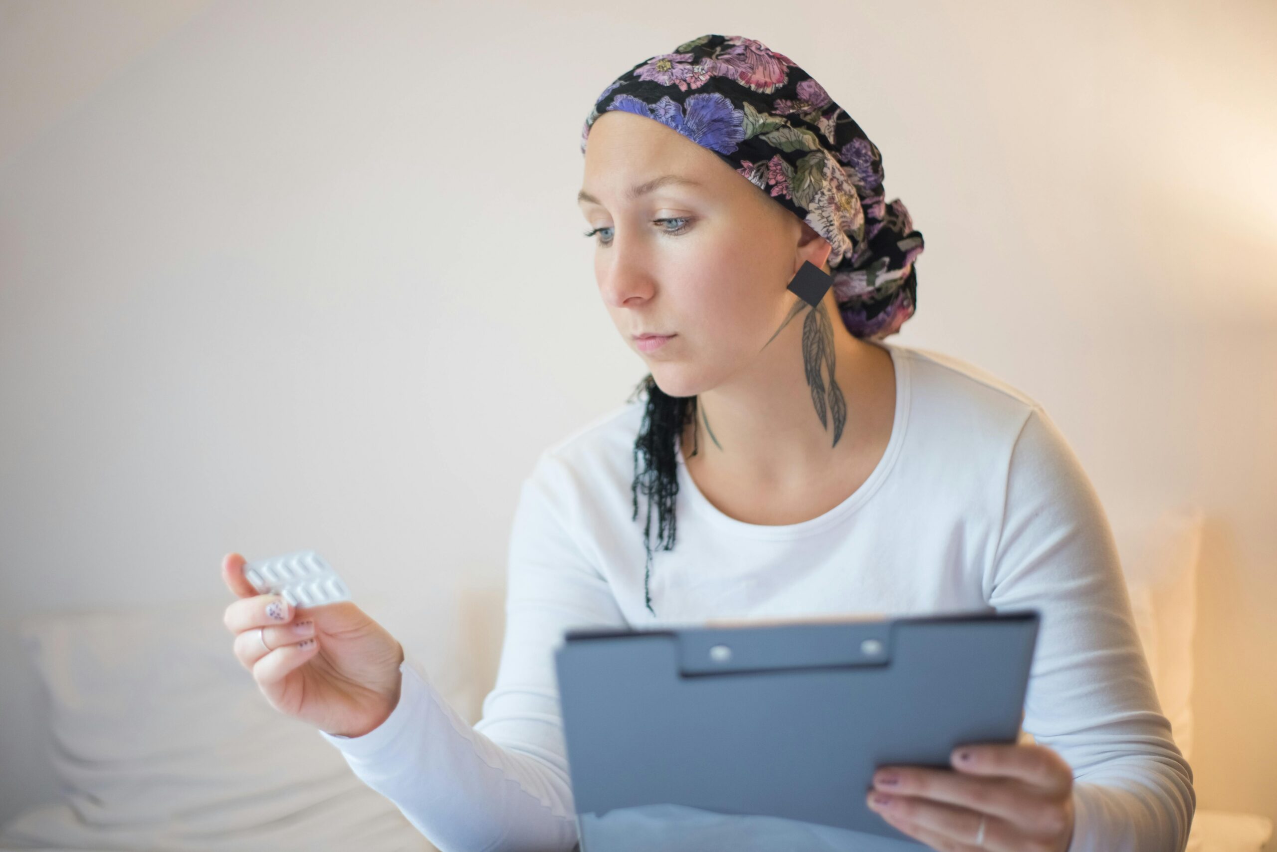 A woman wearing a headscarf, holding a folder in one hand and looking at a blister pack of medication in the other.