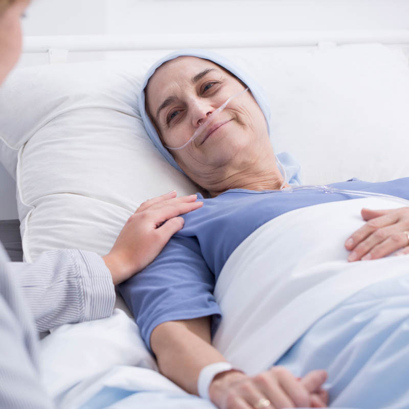 A woman in a hospital gown laying under a blanket in a hospital bed.